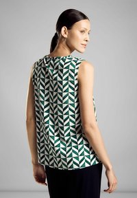 Top senza maniche con un motivo geometrico in verde, bianco e nero; presenta un collo rotondo e un orlo curvo. Tessuto di texture liscia.