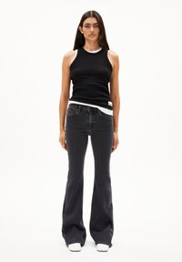 Zwarte geribbelde tanktop over een witte T-shirt, gecombineerd met donkergrijze flared jeans en witte haksandalen. Eenvoudig ontwerp, nauwsluitende pasvorm.