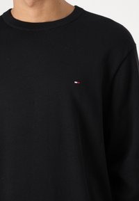Camicia nera in cotone a maniche lunghe con scollo rotondo e un piccolo logo multicolore sul petto sinistro. Tessuto liscio di peso medio.