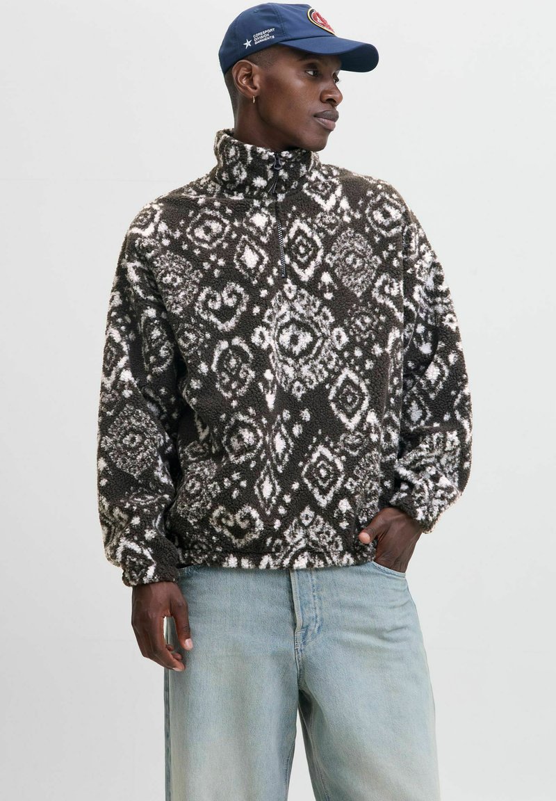 Brun og hvid fleece pullover med højt krave, lynlås og diamantmønstre. Kombineret med lyseblå jeans.