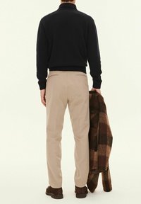 Marinblå stickad tröja, beige byxor och en brun rutig kappa som hålls i handen. Anmärkningsvärda texturer: ribbade muddar och krage, slät tyg av byxorna.