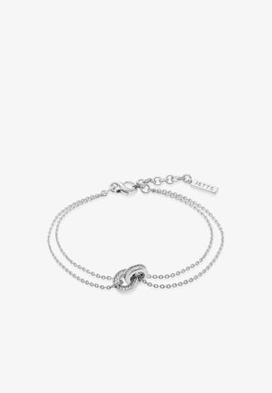 Bracelet délicat en argent à double chaîne avec deux maillons circulaires entrelacés, dont l'un est incrusté de petites pierres claires, et un fermoir avec une étiquette "JETTE".