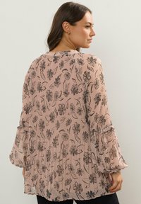 Blush pink bluse med sort blomstermønster, tekstureret stof, lange klokkeærmer og volan detaljer ved ærmerne og nederste kant.