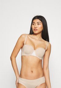 Beige padded bra with thin straps, seamless design, and slight sheen. Paired with matching beige panties featuring a subtle logo.