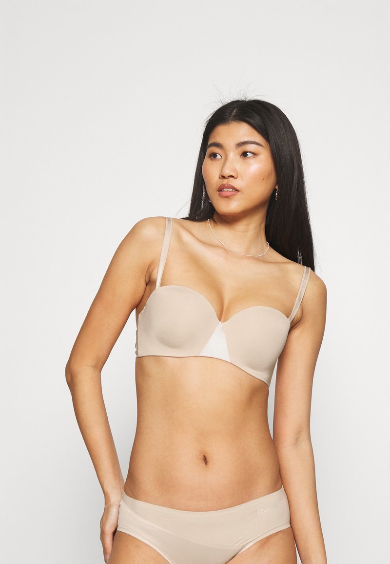 Beige padded bra with thin straps, seamless design, and slight sheen. Paired with matching beige panties featuring a subtle logo.