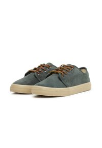 Sneakers in suede verde scuro con suole in gomma beige, punta tonda e stringhe marroni. Texture liscia con design minimalista e senza branding visibile.