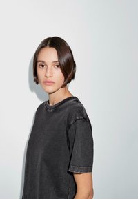 T-shirt nera a maniche corte con scollatura rotonda e leggera texture sfumata. Vestibilità casual, presentata su uno sfondo grigio chiaro.