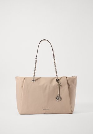 Sac tote rectangulaire beige avec des bretelles en chaîne et un pendentif rond en métal avec le logo MK suspendu à l'avant.