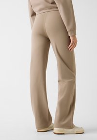 Beżowe, dopasowane spodnie dresowe o miękkiej fakturze, z wysokim stanem i prostym krojem nogawek. Noszone z kremowymi tenisówkami.