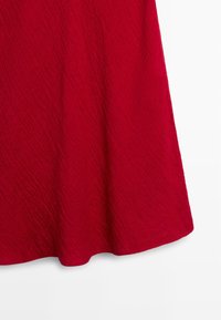 Czerwony tkanina o fakturze zwisająca w dół z delikatną falą wzdłuż dolnej krawędzi na białym tle.