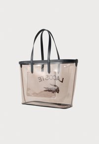Prozirna torba s crnim ručkama, napravljena od prozirnog materijala. Sadrži Lacoste logo i malu torbicu sa patentnim zatvaračem unutar.