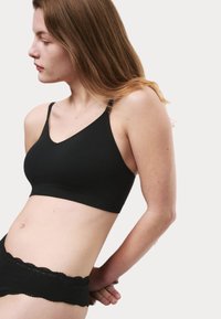 Bralette negro sin costuras con un diseño de escote en V, tirantes ajustables y una textura suave. Combinado con pantalones cortos negros con bordes de encaje.