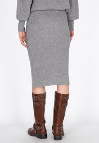 Grauer, gerippter Strickrock mit taillierter Silhouette, kombiniert mit kniehohen, braunen Lederstiefeln mit mehreren Schnallen und strukturiertem Finish.