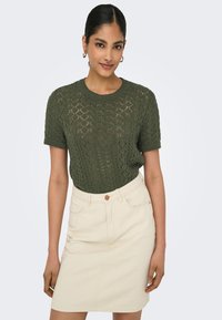 Olive green short-sleeve knit sweater with a diamond pattern, paired with a light beige denim skirt featuring front pockets and button closure.