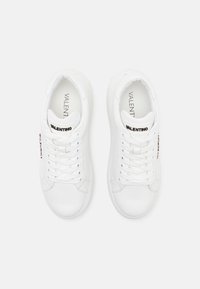 White leather sneakers featuring a rounded toe, laces, and a logo on the tongue. Smooth texture with minimalistic design and understated branding.
