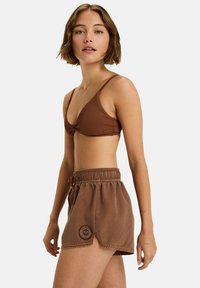 Brauner, gerippter Bikini-Oberteil mit geknoteter Vorderseite, kombiniert mit passenden braunen Shorts mit elastischem Bund und Logo-Patch.