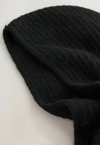 Schwarze Strickmütze aus strukturiertem Stoff mit einem gerippten Muster. Das Material wirkt weich und leicht flauschig, mit einer lockeren Passform.