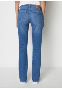 Blå denimjeans med rak bendesign, fem fickor och en brun läderlapp vid baksidan av midjan. Slät textur, mellan tvätt.