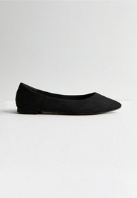 Zapato plano de ante negro con punta afilada, tacón bajo y textura suave. Sin herrajes visibles ni patrones. Diseño simple y minimalista.