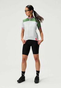 Krátky rukáv cyklistický dres svetlošedej a zelenej farby so zipsom vpredu, v kombinácii s čiernymi šortkami. Obsahuje čierne cyklistické topánky a patterned ponožky.