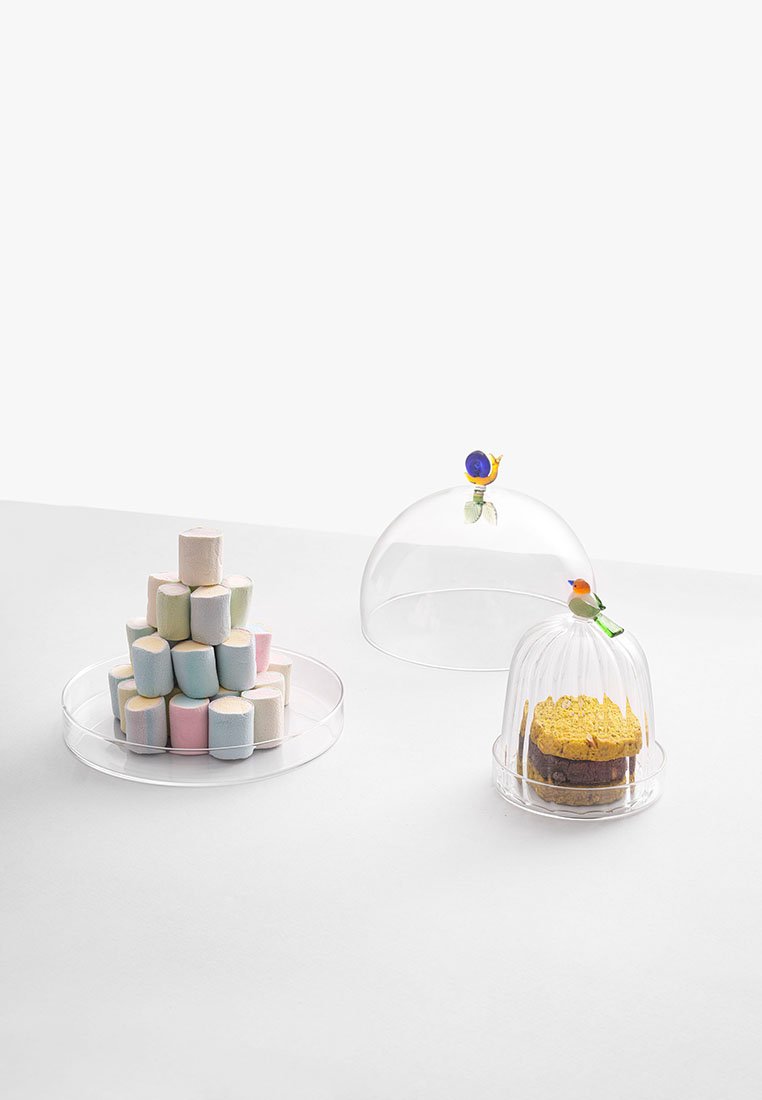 Trzy przezroczyste, kopułowe pokrywy na jedzenie prezentują pastelowe pianki marshmallow ułożone w piramidę oraz warstwowy tort ozdobiony dekoracyjnym akcentem.