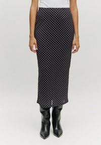 Schwarzer Midirock mit weißen Punkten, der eine figurbetonte Silhouette und eine glatte Textur aufweist, kombiniert mit schwarzen knielangen Stilettos.