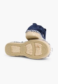 Chaussure en toile navy avec une semelle en jute tressé, des coutures blanches et un design en tissu texturé. Présente un bout arrondi et des bords supérieurs doux.