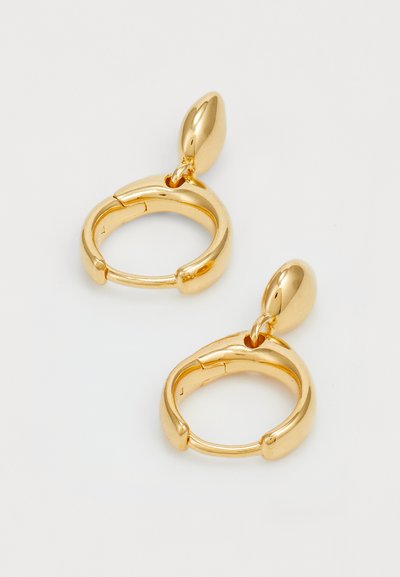 Boucles d'oreilles créoles en or avec un design lisse et arrondi, agrémentées d'un petit accent ovale sur le dessus et d'une texture brillante.
