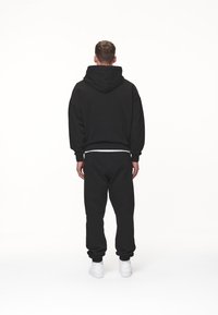 Sudadera con capucha negra y pantalones de chándal a juego, hechos de un tejido suave, con puños elásticos y un corte relajado. Zapatillas blancas completan el look.