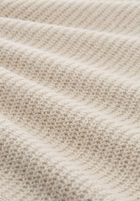Beige gebreide stof met een getextureerd, ribbelpatroon en zachte, multidirectionele lijnen. Het materiaal lijkt warm en uitnodigend.