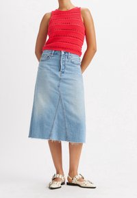 Punat virkattu toppi, jossa on teksturoitu kuvio, ja vaaleansiniset farkkuhameet, joissa on etusauma ja risat helmat. Yhdistetty valkoisiin korkokenkiin.