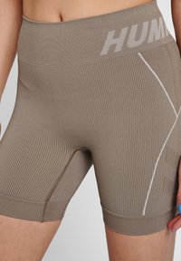 Bruna idrottsshorts med ribbad textur, bred midjeband och "HUM"-logga; har vita detaljer och en åtsittande design.