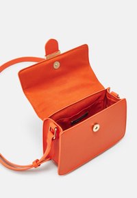 Sac bandoulière en cuir orange avec une fermeture à pression magnétique et une seule sangle ; l'intérieur est doté d'une doublure lisse et d'une étiquette de marque.