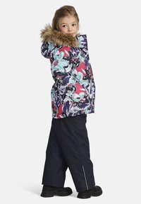 Blommönstrad vinterjacka med pälskantad huva, i kombination med marinblå skidbyxor. Har dragkedjestängning och sidfickor.