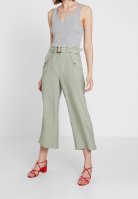 Grå ribbad tanktop med v-ringad hals, matchad med ljusgröna vida byxor med framfickor och ett bälte. Röda sandaletter med remmar och klack.