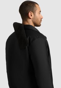 Jachetă neagră cu un guler moale, texturat. Prezintă un design dintr-un material neted, buzunare laterale și umeri structurați pentru o potrivire modernă.