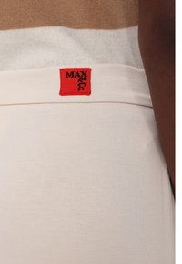 Gros plan sur la ceinture d'un pantalon beige avec une petite étiquette en tissu rouge cousue dessus affichant un texte noir.