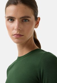 T-shirt en coton vert avec un col rond. Présente une texture douce et un design ajusté, avec des coutures subtiles au niveau des épaules.