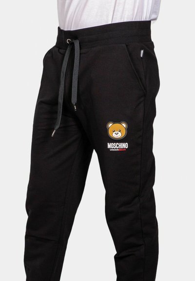 Pantaloni sportivi neri con vita regolabile, caratterizzati da una grafica di un orso e dal logo "Moschino Underbear" sulla coscia sinistra. Texture in morbido cotone.