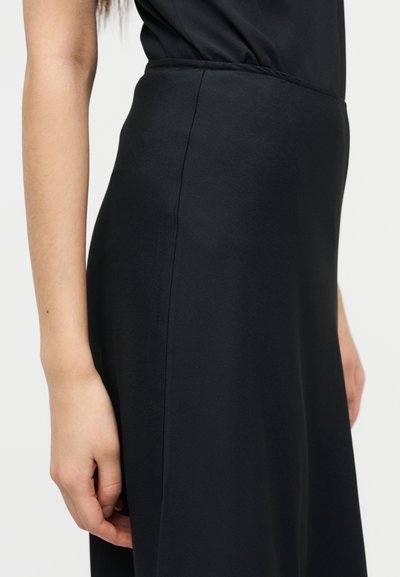 Μαύρο φόρεμα με λείο, ματ ύφασμα. Κοντινή λήψη στην περιοχή της μέσης που δείχνει μια ορισμένη ραφή και διακριτικό πιέτες. Απλός σχεδιασμός χωρίς σχέδια.