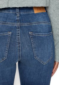 Jeans de denim azul con un diseño ajustado, dos bolsillos traseros y costuras visibles. Presenta una etiqueta de cuero en la cintura.