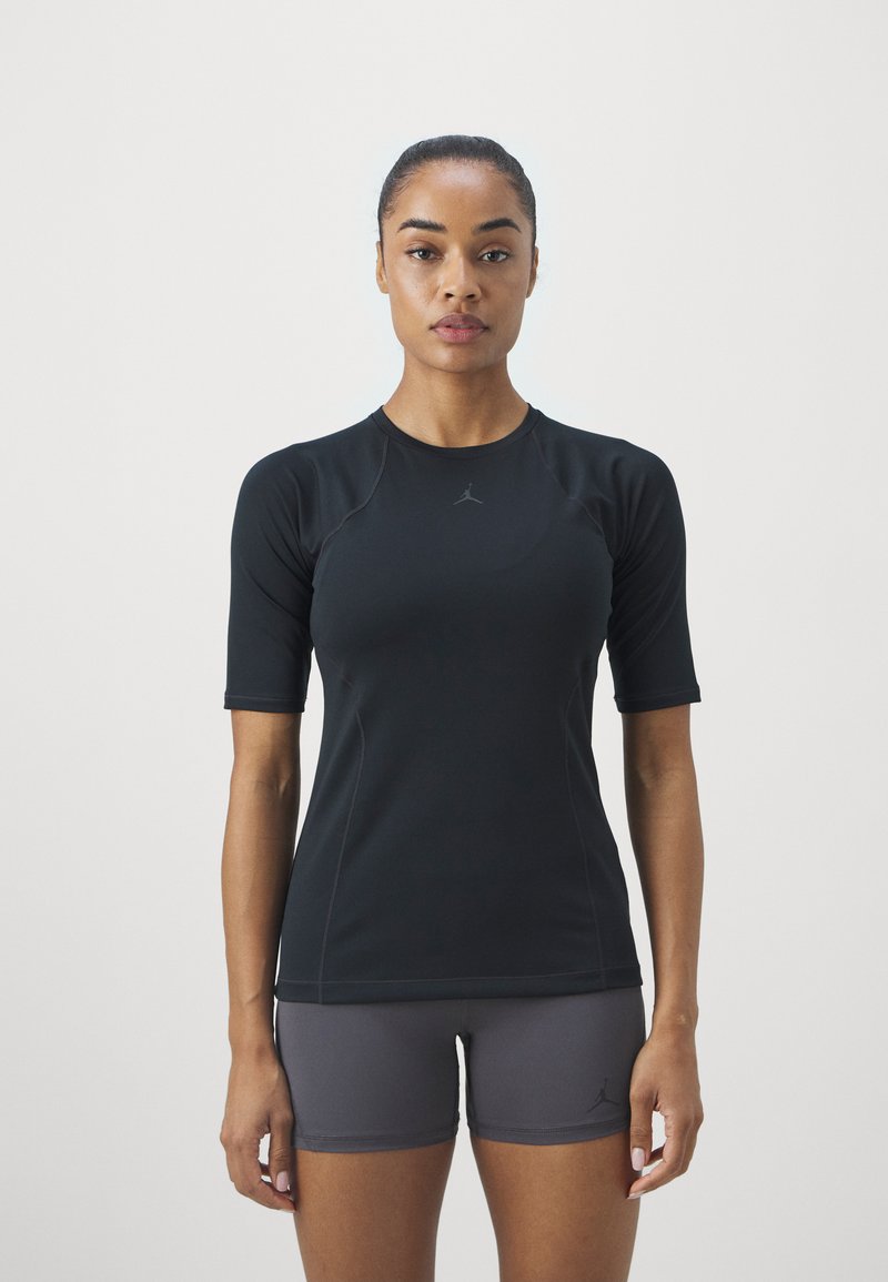 Camiseta atlética negra de manga corta con mangas raglán, que presenta un logo sutil y una textura suave, combinada con pantalones cortos grises.