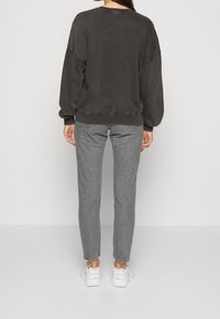 Tmavě šedá oversized mikina s kleslými rameny, žebrovanými manžetami a lemem; v kombinaci se slim-fit šedými džíny a bílými teniskami.