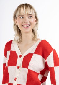 Piros-fehér kockás kardigán, V-nyakú dizájn, texturált kötés, három piros gomb a frontra, puha anyag, laza szabású.