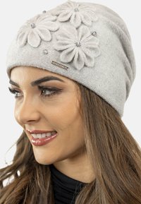 Berretto lavorato a maglia grigio con tre fiori in feltro e accenti di cristallo, vestibilità aderente e lavorazione a coste discreta per una maggiore texture. Piccola etichetta con logo visibile.