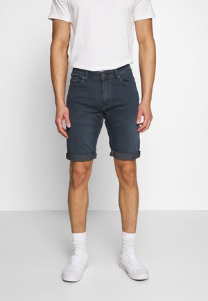 Dunkelblaue Jeansshorts mit schlanker Passform, umgeschlagenen Säumen und fünf Taschen, kombiniert mit einem schlichten weißen T-Shirt und weißen Sneakers.