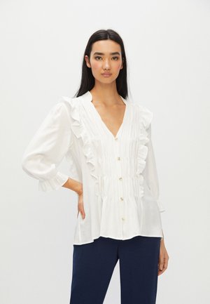 Weißes Blusenshirt mit Rüschenverzierungen, V-Ausschnitt und Knopfverschluss. Weicher Stoff, lange Ärmel mit gerafften Manschetten und lockerer Passform.