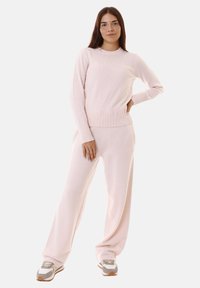 Maglione rosa chiaro e pantaloni larghi coordinati in morbido tessuto a maglia, con polsini e vita a coste, indossati con sneakers grigie e bianche.