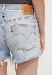 Ljusblå denimshorts med fransade kanter, som har en bakficka och en brun läderetikett med präglade grafiska detaljer.