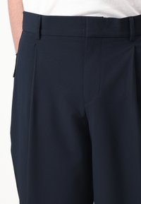Pantalons navy à texture lisse, dotés d'un devant plat, de poches latérales et d'une taille ajustée, conçus pour un look sur mesure.